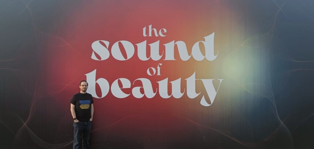 Me standing in front of The Sound of Beauty logo m